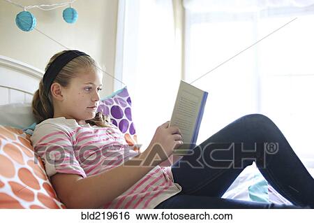 Stock Photograph - Close up of girl reading book on bed. Fotosearch