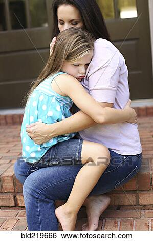 Stock Photograph - Close up of mother comforting daughter on front stoop. Fotosearch