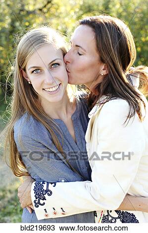 Stock Image - Close up of mother kissing cheek of daughter. Fotosearch