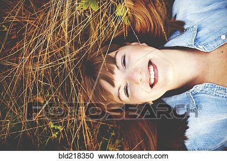 Stock Image - Close up of smiling woman laying in tall grass. Fotosearch