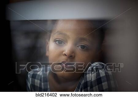Stock Image - Close up of wistful girl looking out window. Fotosearch