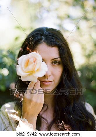 Stock Image - Close up of woman holding rose outdoors. Fotosearch
