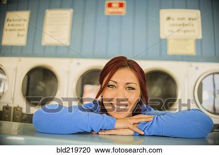 Stock Image - Close up of woman leaning on counter at laundromat. Fotosearch