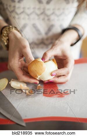 Stock Photography - Close up of woman peeling onion on cutting board. Fotosearch