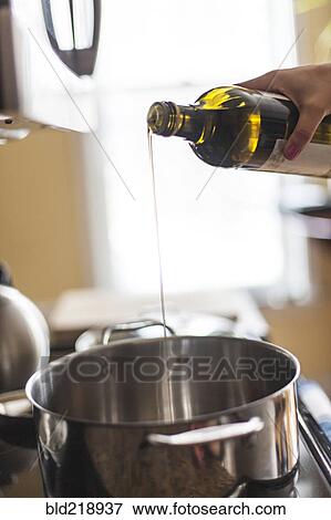 Stock Photo - Close up of woman pouring olive oil into pot. Fotosearch