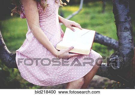 Stock Image - Close up of woman reading book in tree. Fotosearch