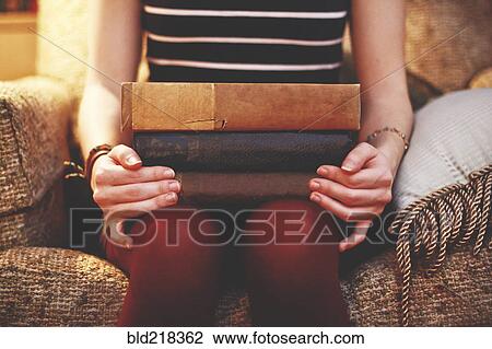 Stock Image - Close up of woman sitting on armchair holding books. Fotosearch