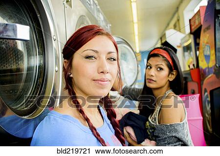 Stock Image - Close up of women washing clothes at laundromat. Fotosearch