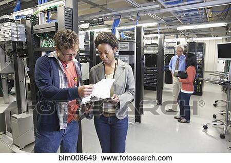 Stock Photo - Co-workers looking at clipboard in office technology room. Fotosearch