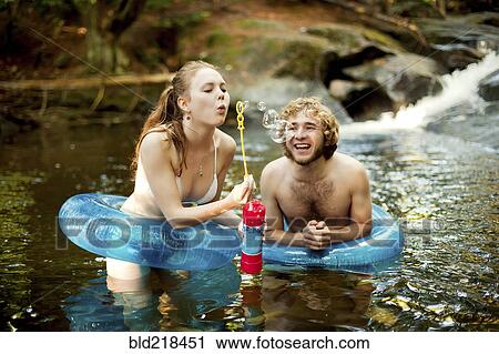 Stock Image - Couple blowing bubbles in forest river. Fotosearch