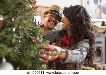 Stock Image - Couple decorating Christmas tree. Fotosearch