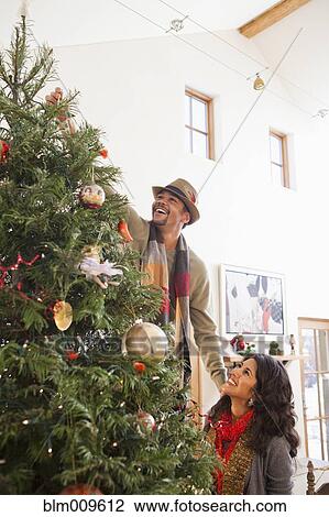 Stock Image - Couple decorating Christmas tree together. Fotosearch