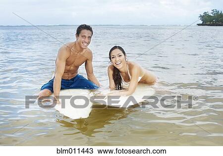 Stock Image - Couple floating in ocean on surfboards. Fotosearch