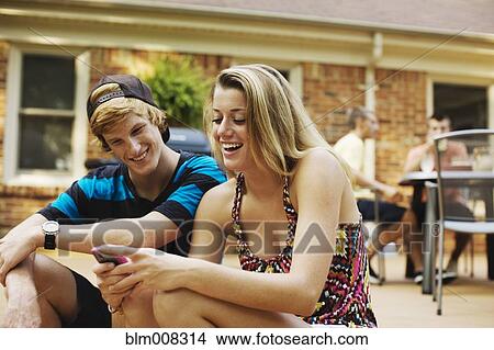 Picture - Couple hanging out together on patio looking at cell phone. Fotosearch