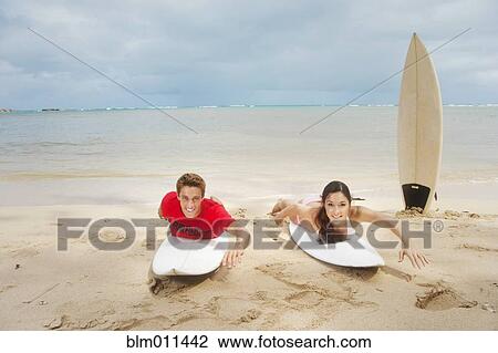 Stock Image - Couple laying on surfboards on beach. Fotosearch