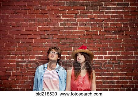 Stock Image - Couple leaning on brick wall. Fotosearch