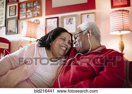 Stock Image - Couple listening to earbuds in living room. Fotosearch