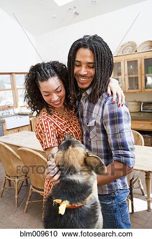 Stock Image - Couple petting dog in kitchen. Fotosearch