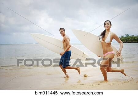 Stock Photography - Couple running on beach carrying surfboards. Fotosearch