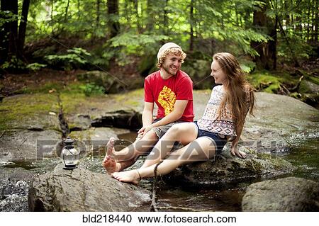 Stock Image - Couple sitting barefoot on boulders in forest. Fotosearch