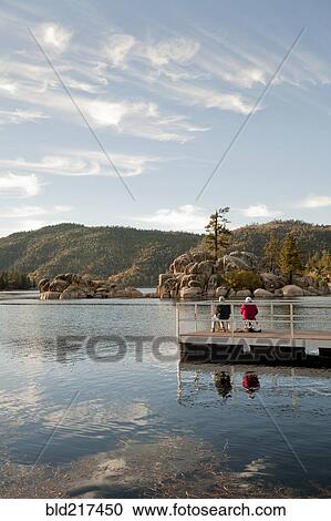 Stock Image - Couple sitting on wooden deck in remote lake. Fotosearch