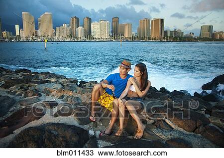 Stock Image - Couple sitting together on rocky shore. Fotosearch