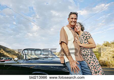 Couple smiling near classic convertible View Large Photo Image Stock Photograph - Couple smiling near classic convertible. Fotosearch