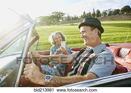 Stock Image - Couple taking cell phone photograph in classic convertible. Fotosearch