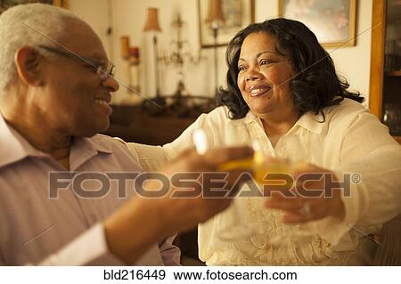 Couple toasting each other with wine in living room View Large Photo Image Stock Photo - Couple toasting each other with wine in living room. Fotosearch