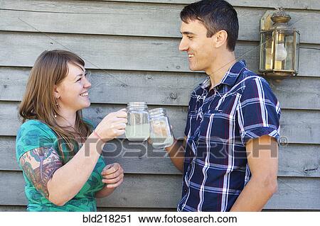 Stock Image - Couple toasting with drinks near wall. Fotosearch