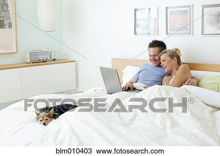Couple using laptop together in bed View Large Photo Image Stock Image - Couple using laptop together in bed. Fotosearch
