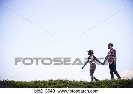 Couple walking together in grassy field View Large Photo Image Stock Image - Couple walking together in grassy field. Fotosearch