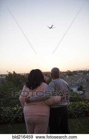 Stock Photo - Couple watching airplane flying over cityscape. Fotosearch