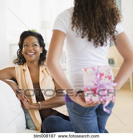 Stock Photo - Daughter holding birthday gift behind back for mother. Fotosearch