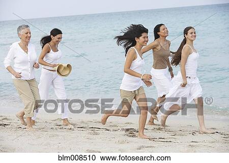 Stock Image - Diverse women running on beach together. Fotosearch