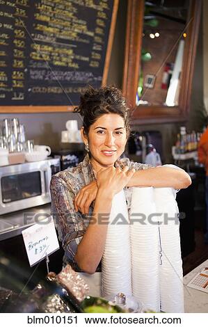 Stock Image - Ecuadorian business owner standing with disposable cups in cafe. Fotosearch