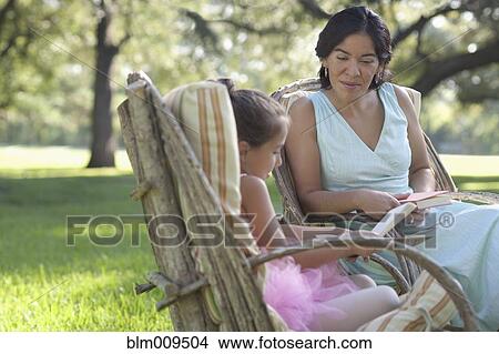 Picture - Elegant mother and daughter reading books in backyard. Fotosearch