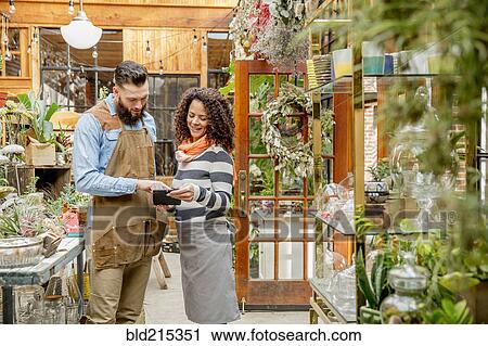 Stock Image - Employees using digital tablet in plant nursery. Fotosearch
