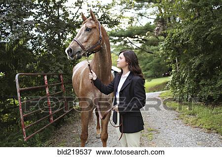 Stock Photo - Equestrian woman walking horse on dirt path. Fotosearch