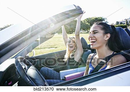 Stock Image - Excited women driving convertible on road trip. Fotosearch