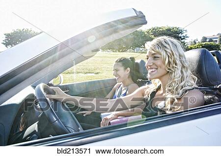 Stock Image - Excited women driving convertible on road trip. Fotosearch