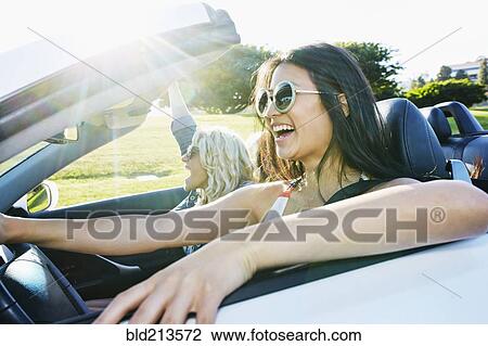 Stock Image - Excited women driving convertible on road trip. Fotosearch