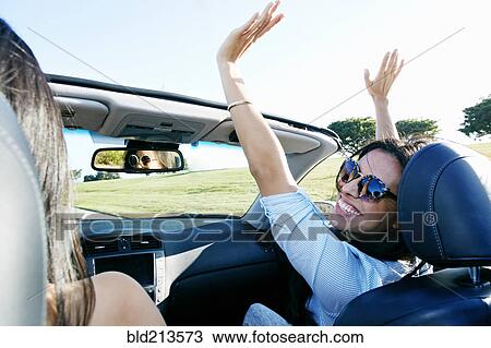 Stock Image - Excited women driving convertible on road trip. Fotosearch