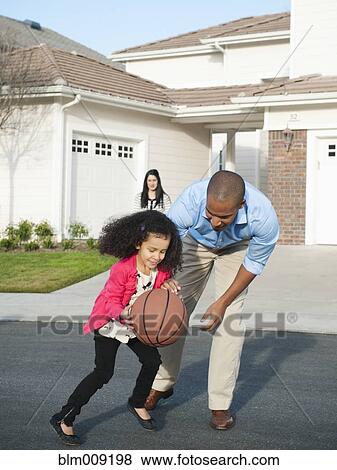Stock Photo - Father and daughter playing basketball in road. Fotosearch