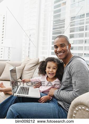 Stock Image - Father and daughter using laptop on sofa. Fotosearch