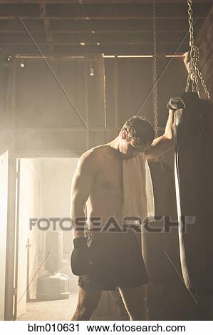 Stock Image - Fatigued boxer leaning on punching bag. Fotosearch