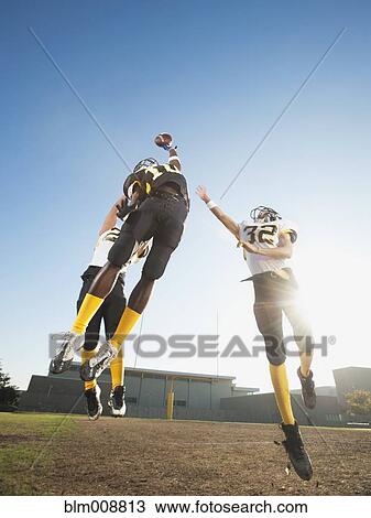 Stock Image - Football player catching ball on football field. Fotosearch