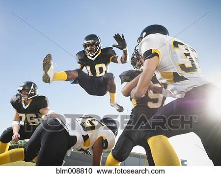 Stock Image - Football player leaping over players on football field. Fotosearch