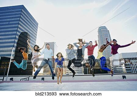 Stock Image - Friends jumping for joy on urban rooftop. Fotosearch