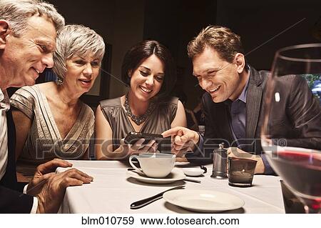 Friends looking at camera phone in restaurant View Large Photo Image Stock Photo - Friends looking at camera phone in restaurant. Fotosearch